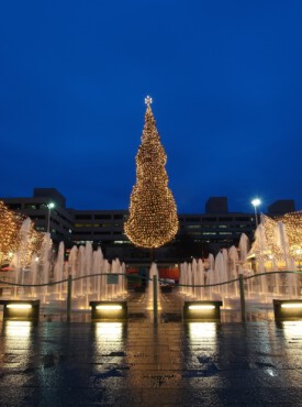 Crown Center plaza at night with a large illuminated Christmas tree, light-wrapped trees, and water fountains